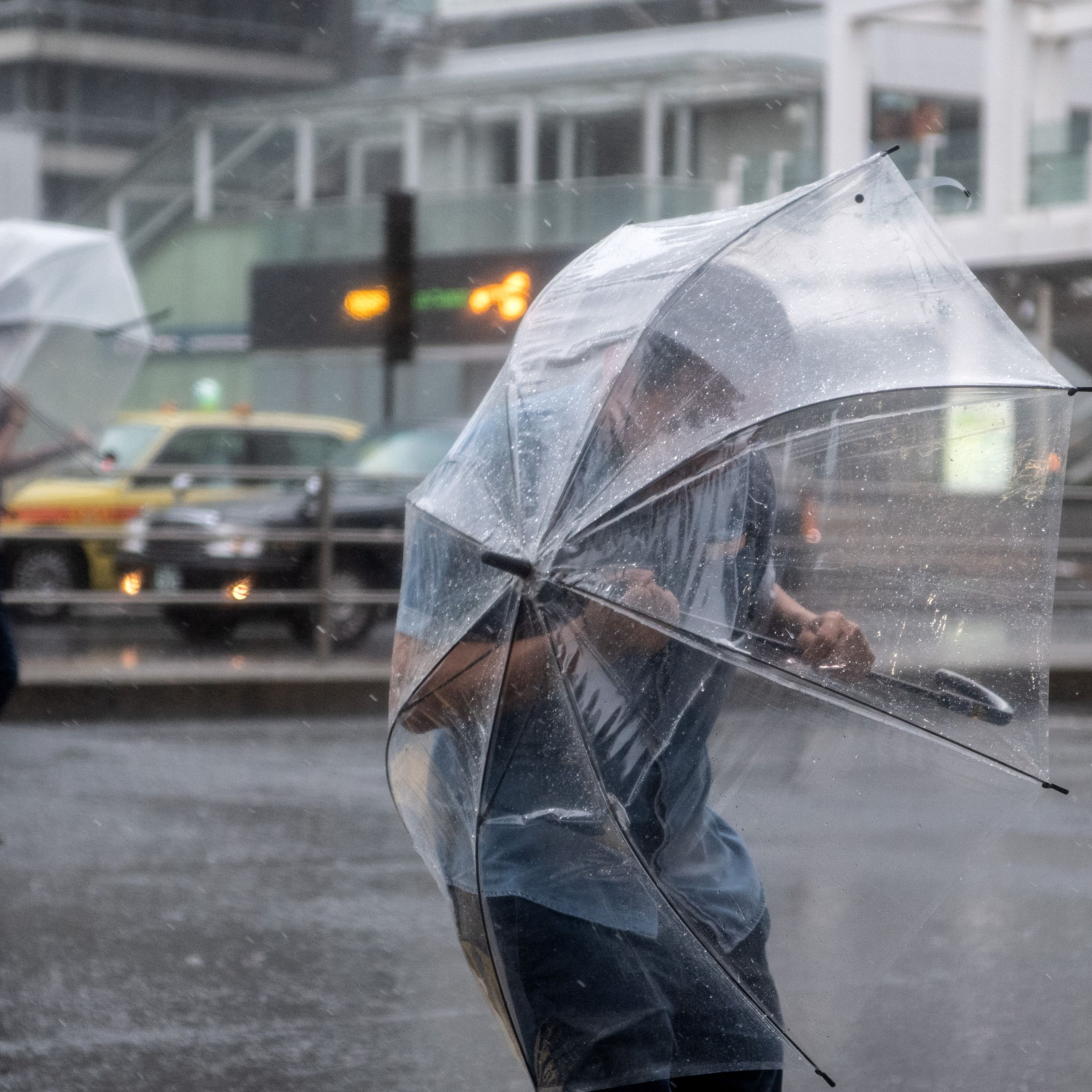 Two people standing in a street shield themselves from rain and snow with clear umbrellas.