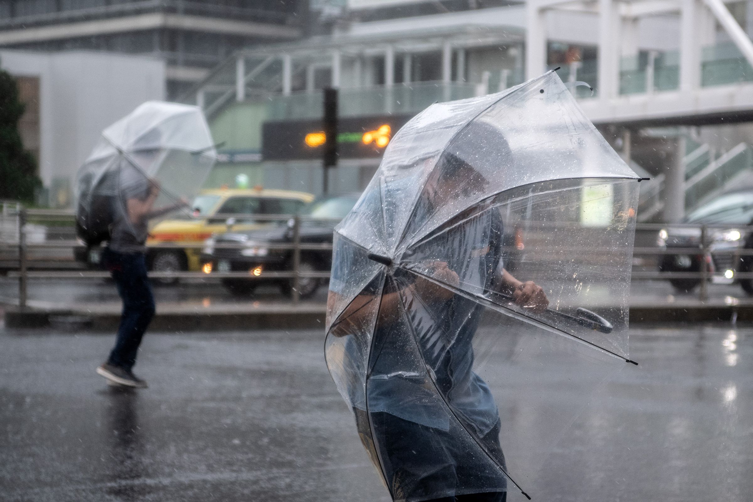 Two people standing in a street shield themselves from rain and snow with clear umbrellas.