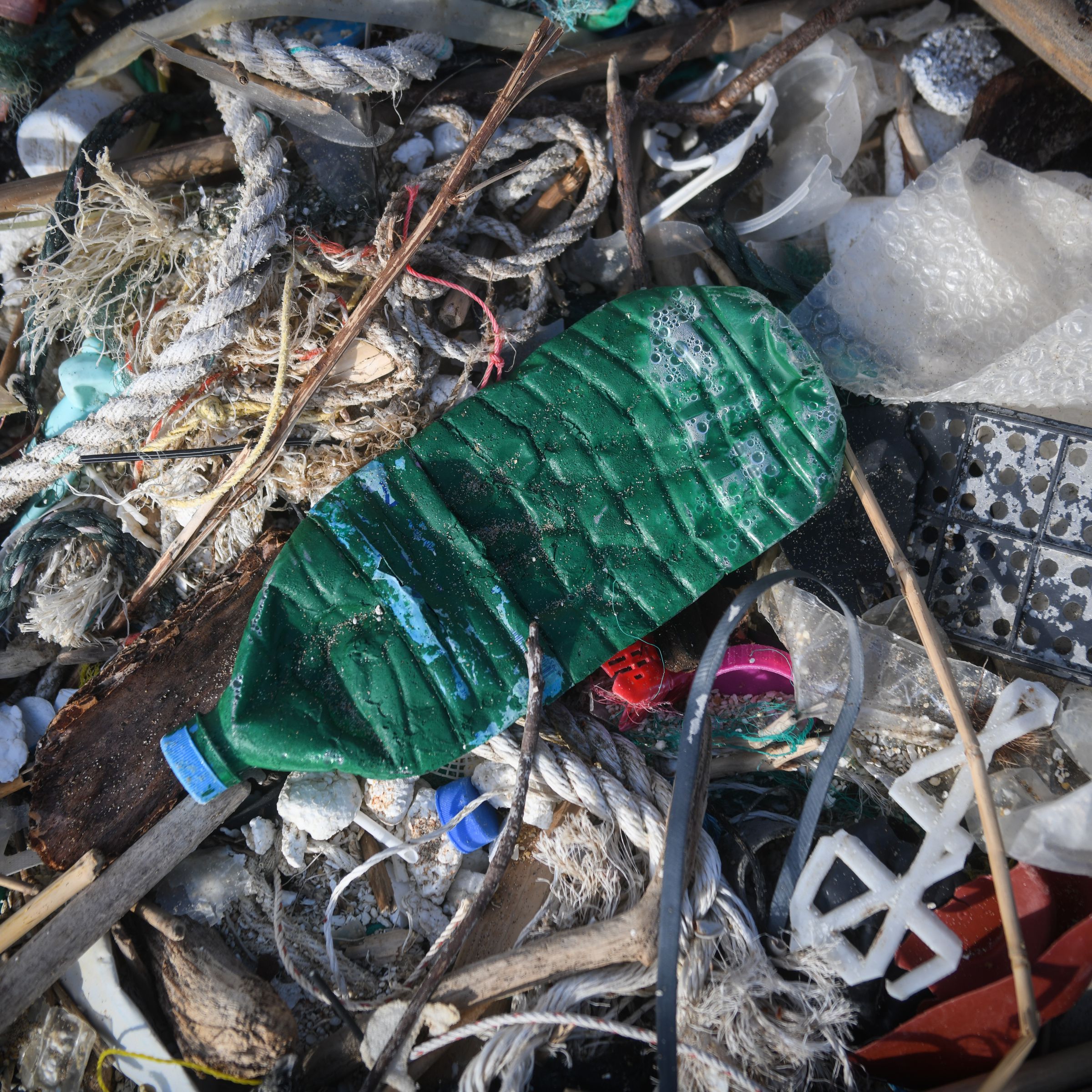 A close-up of a pile of garbage, including a plastic beverage bottle, bubble wrap, rope, and string.