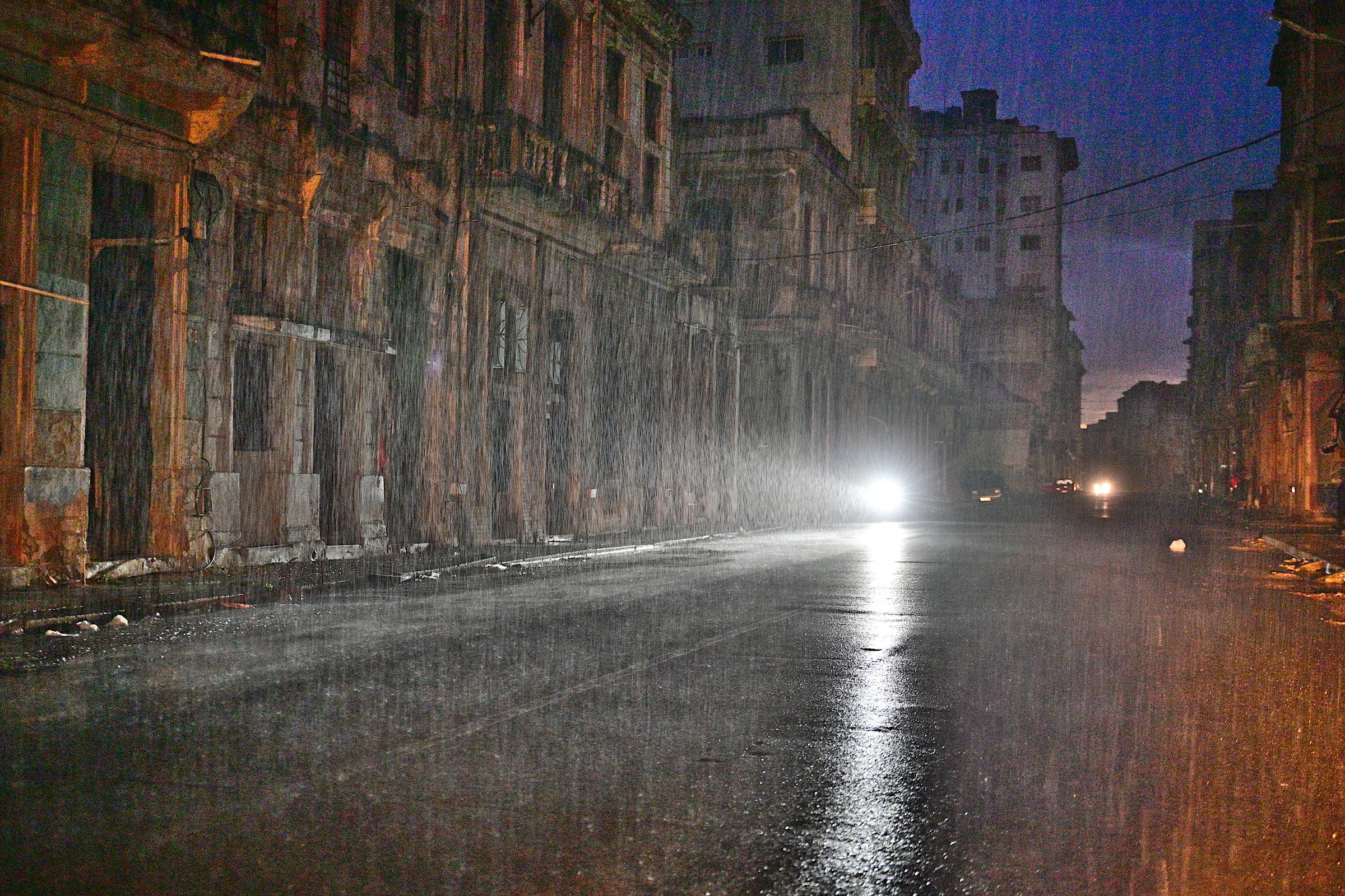 A motorcycle drives along a city street under pouring rain. 