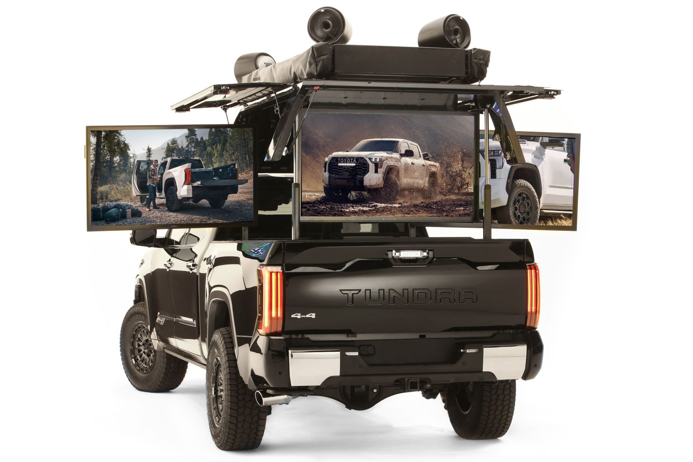rear of black pickup truck with five TVs fanned out from the bed and a canopy with speakers up top.